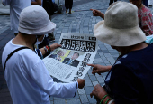 People react as they read a special edition of Yomiuri Shimbun newspaper reporting the tariff deal agreement between U.S and Japan, in Tokyo