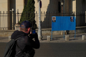 A man takes a photo of electoral posters of Nicusor Dan and George Simion in Bucharest