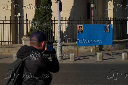 A man takes a photo of electoral posters of Nicusor Dan and George Simion in Bucharest