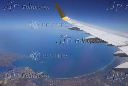An aerial view through the window of a passenger aircraft shows the coast in front of the Ionian Sea, in Taranto