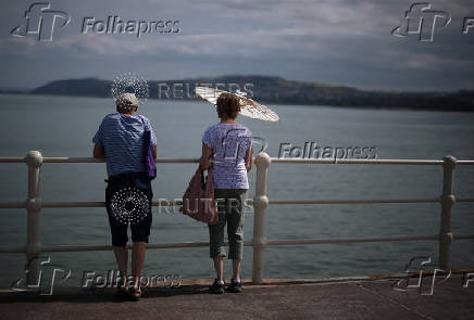 A woman uses a parasol to shelter from the sun on the promenade at Rhos-on-Sea, Wales