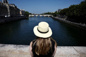 A woman looks at the River Seine from a bridge on a warm and sunny spring day in Paris