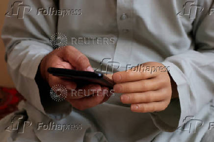 Man with a prosthetic hand, produced by the Bioniks Private Limited, uses a mobile phone at home in Karachi