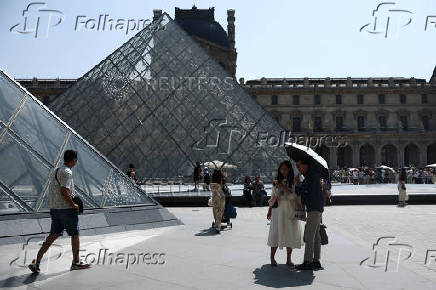 People in front of the glass Pyramid of the Louvre museum on a warm and sunny day in Paris