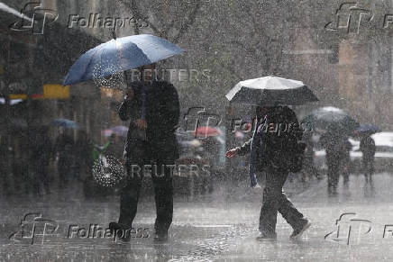 People use umbrellas to shelter from the rain as they walk along Pitt Street mall