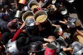 Palestinians wait to receive food cooked by a charity kitchen, in Khan Younis