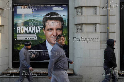 Three men pass by a poster of Nicusor Dan in Bucharest