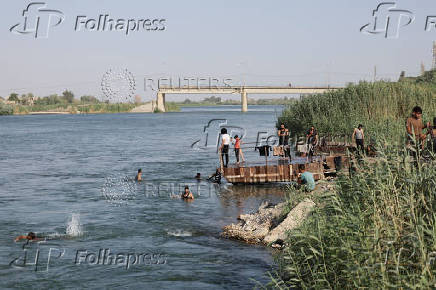 People swim in the river, with the damaged bridge visible in the background, in Deir El-Zor