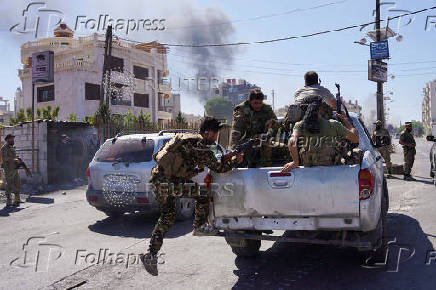 Smoke rises as Syrian security forces ride on a back of a truck after Syrian troops entered the predominantly Druze city of Sweida