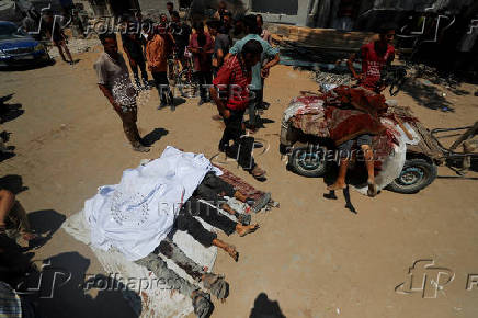 People stand near the bodies of Palestinians, who were killed by Israeli fire while seeking aid in northern Gaza, according to medics, in Gaza City