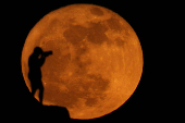 A photographer is silhouetted against the full moon known as the strawberry moon in Arinaga