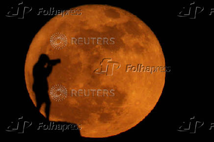 A photographer is silhouetted against the full moon known as the strawberry moon in Arinaga