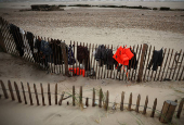 Items of clothing and life jackets left behind by migrants trying to cross the English Channel hang from a fence on the beach in Wimereux