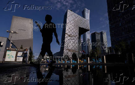 A man is reflected in a puddle as he walks past the CCTV building in Central Business District of Beijing