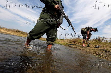A soldier from the Kachin Independence Army puts on his shoes as he and his comrade cross a stream towards the front line in Laiza