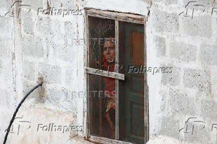 Woman looks out from a window of her home in Chakothi Village