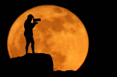 A photographer is silhouetted against the full moon known as the strawberry moon in Arinaga