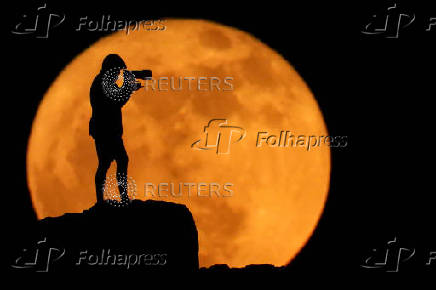 A photographer is silhouetted against the full moon known as the strawberry moon in Arinaga