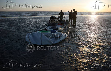 Police officers examine the motor on a dinghy after it was abandoned by migrants trying to cross the English Channel on a beach at Gravelines