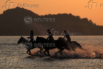 People ride horses during sunset as temperatures rise near Durres