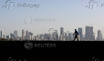 FILE PHOTO: FILE PHOTO: A man walks along a wall overlooking the central Mumbai's financial district skyline
