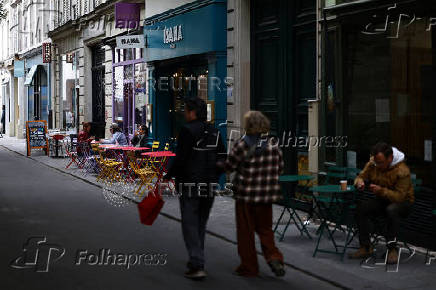 People walk past cafe terraces in a street in Paris