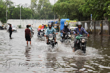 Commuters ride motorbikes through flooded streets following torrential rains, in Ahmedabad