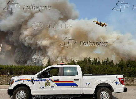 Water bomber flies over the plume of smoke from a wildfire near The Pas