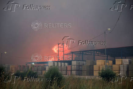 Flames rise from a cement factory sparked by a nearby wildfire, in Patras