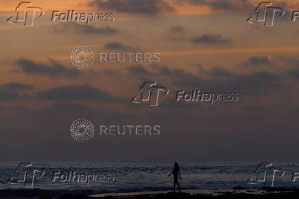 A swimmer heads into the ocean after sunset in California