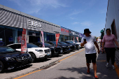 People walk past second hand vehicles and dealerships at a used car market in Beijing