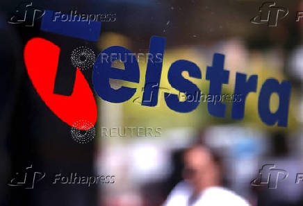 FILE PHOTO: A pedestrian walks past a Telstra logo adorning a phone booth in the central business district of Sydney