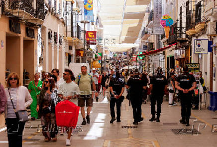 FILE PHOTO: Spanish national police officers walk past tourists as they patrol a shopping street in Ronda