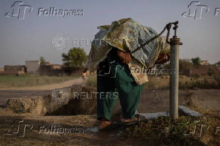 Woman takes drink from water well during heatwave in Daska