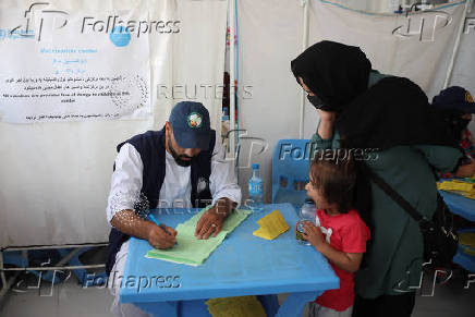 An Afghan woman, who was deported from Iran, registers her daughter for vaccination inside a WHO tent at a camp for returning migrants near the Islam Qala border crossing