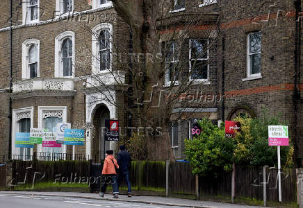 FILE PHOTO: People walk past estate agent signs along a residential street in South London