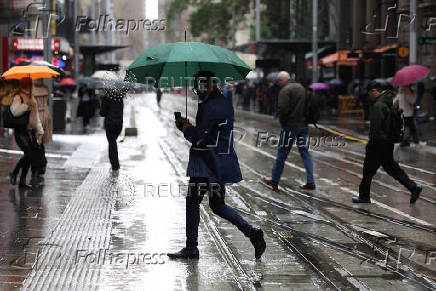 People use an umbrellas to shelter from the rain as they cross the street in Syndey