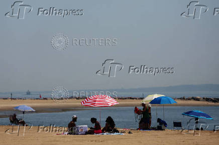 People sit on the beach during a heatwave in the Bronx borough of New York City