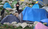 A migrant walks towards tents in a small camp carrying food distributed by a charity in Calais, France