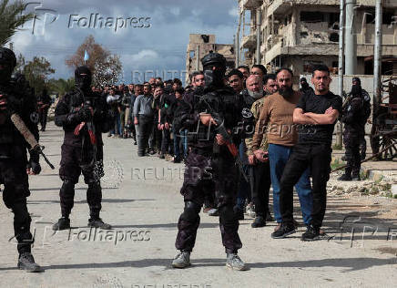 Soldiers from the Syrian Democratic Forces stand in front of the detainees in Aleppo