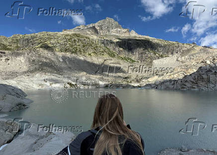 A woman takes a picture at lake at the bottom of the Rhone glacier amid climate change in Obergoms