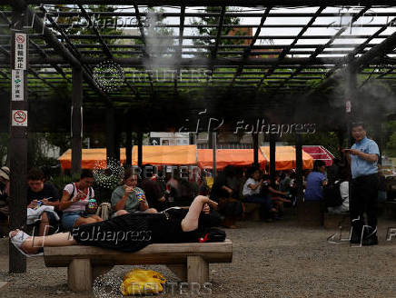 A woman takes a nap underneath cooling mist near a venue of the Hozuki-Ichi (Japanese lantern plant fair), at Sensoji temple, in Tokyo