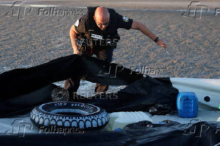 A police officer uses a knife to slash a dinghy after it was abandoned by migrants trying to cross the English Channel on a beach at Gravelines