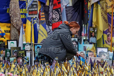 Woman places a flag at the makeshift memorial to fallen Ukrainian defenders at Independence Square in Kyiv