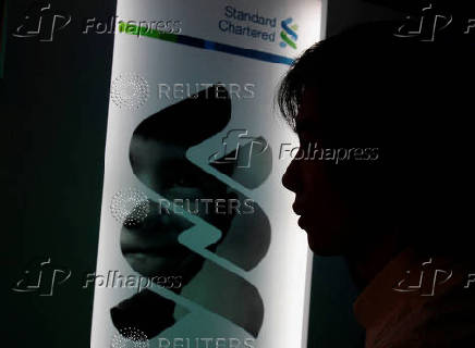FILE PHOTO: A journalist listens in front of a Standard Chartered bank logo during a news conference which announced the bank's results in Hong Kong