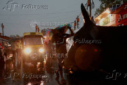 A man uses a cloth to cover himself from the rain as he walks through a wholesale market in, New Delhi