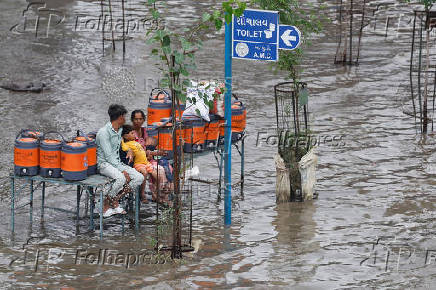 A family sit on the bench of a bus stop surrounded by water containers while waiting for transport, as streets are flooded after torrential rain, in Ahmedabad