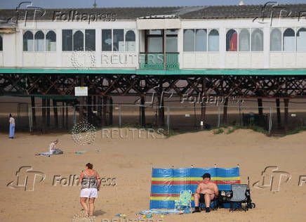 People sit on the beach in front of the pier at St Annes