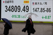 Pedestrians walk past a stock quotation board showing Nikkei share average and exchange rate between Japanese yen and U.S. dollar outside a brokerage in Tokyo