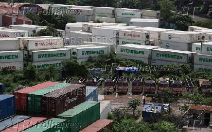 A man walks past trucks and shipping containers at a warehouse in Navi Mumbai